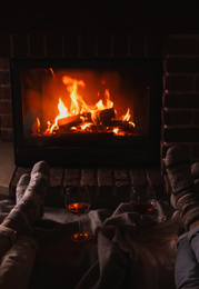 Couple and glasses of red wine near burning fireplace, closeup
