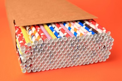 Box with many paper drinking straws on orange background