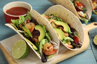 Photo of Delicious tacos with shrimps, avocado and lime on turquoise wooden table, closeup