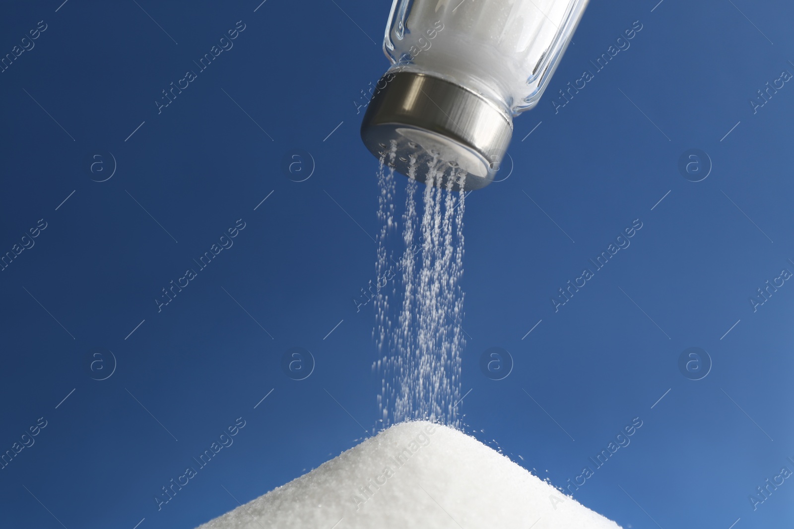 Photo of Pouring salt from shaker on blue background, closeup