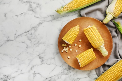 Photo of Plate with tasty sweet corn cobs on marble table, top view