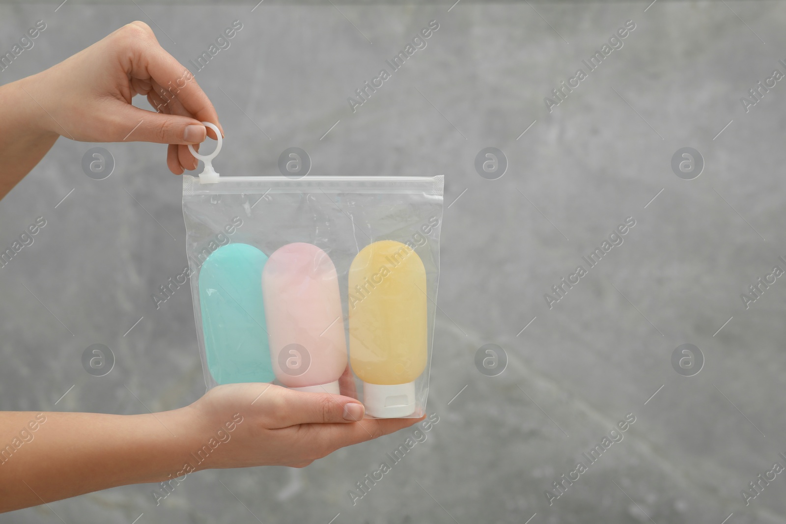 Photo of Woman holding plastic bag of cosmetic travel kit near grey wall, closeup and space for text. Bath accessories
