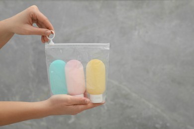 Woman holding plastic bag of cosmetic travel kit near grey wall, closeup and space for text. Bath accessories