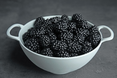 Photo of Colander with tasty ripe blackberries on grey table