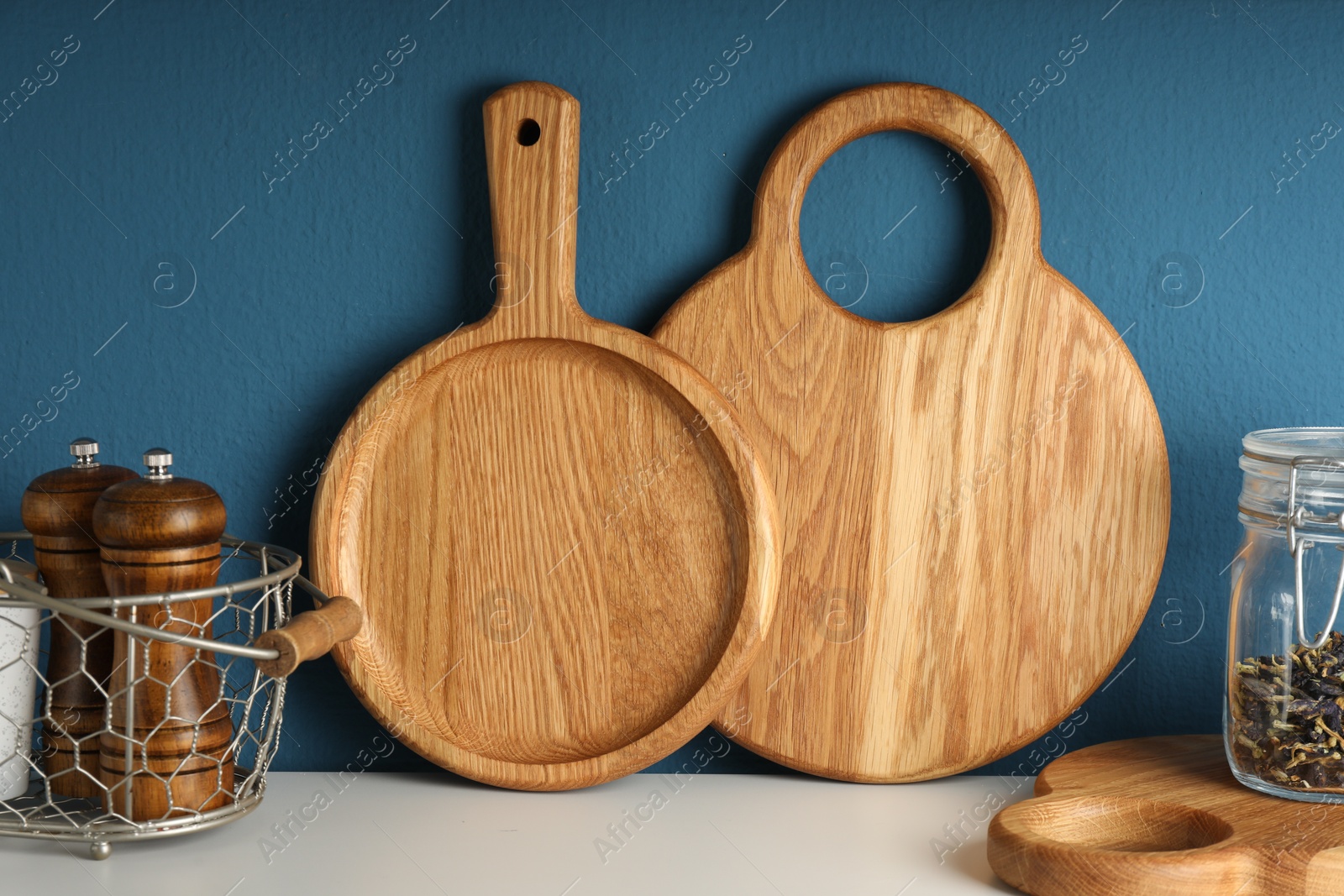 Photo of Wooden cutting boards, shakers and dry tea on white table near blue wall