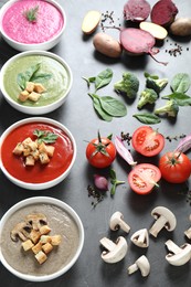 Different tasty cream soups in bowls and ingredients on dark grey table