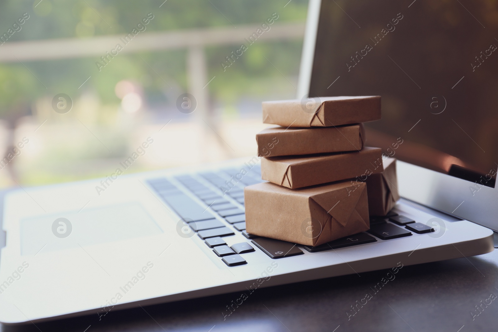 Photo of Internet shopping. Small boxes on modern laptop indoors, closeup with space for text