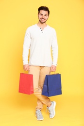 Photo of Full length portrait of young man with paper bags on yellow background