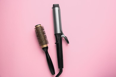 Photo of Hair styling appliance. Curling iron and round brush on pink background, top view