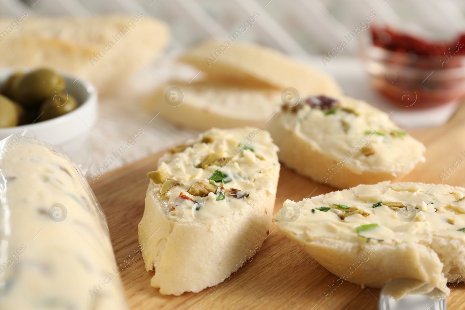 Photo of Tasty butter with olives, green onion and bread on wooden board, closeup