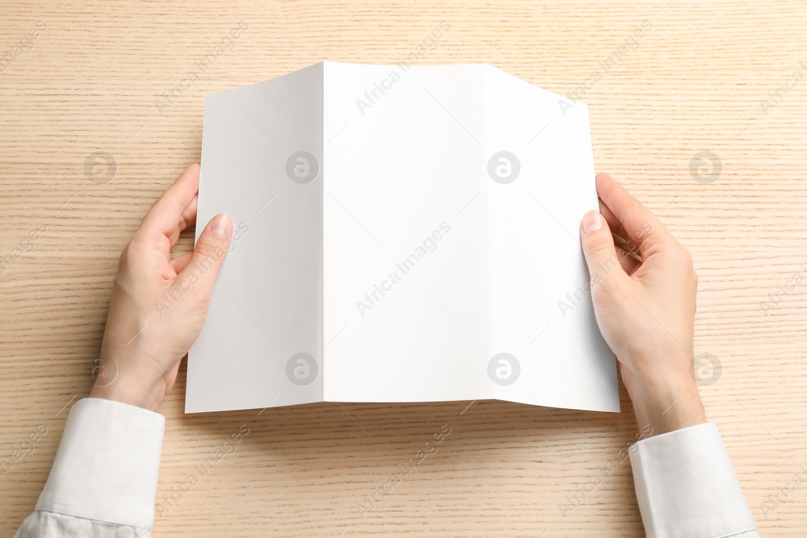 Photo of Young woman holding blank brochure at light wooden table, top view. Mock up for design