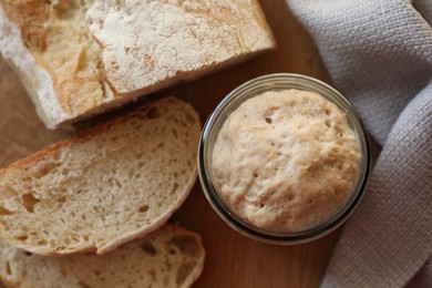 Photo of Sourdough starter in glass jar and bread on wooden table, top view