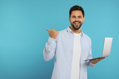 Special promotion. Smiling man with laptop pointing at something on light blue background. Space for text