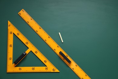 Triangle, ruler and chalk on green chalkboard, flat lay. Space for text