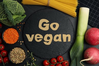 Slate plate with phrase Go Vegan and fresh products on black background, flat lay