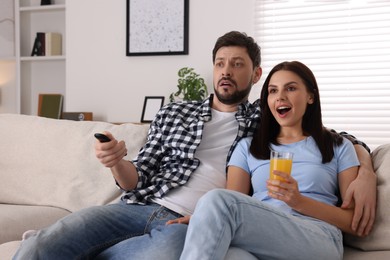 Photo of Shocked couple watching show at home. Man changing TV channels with remote control