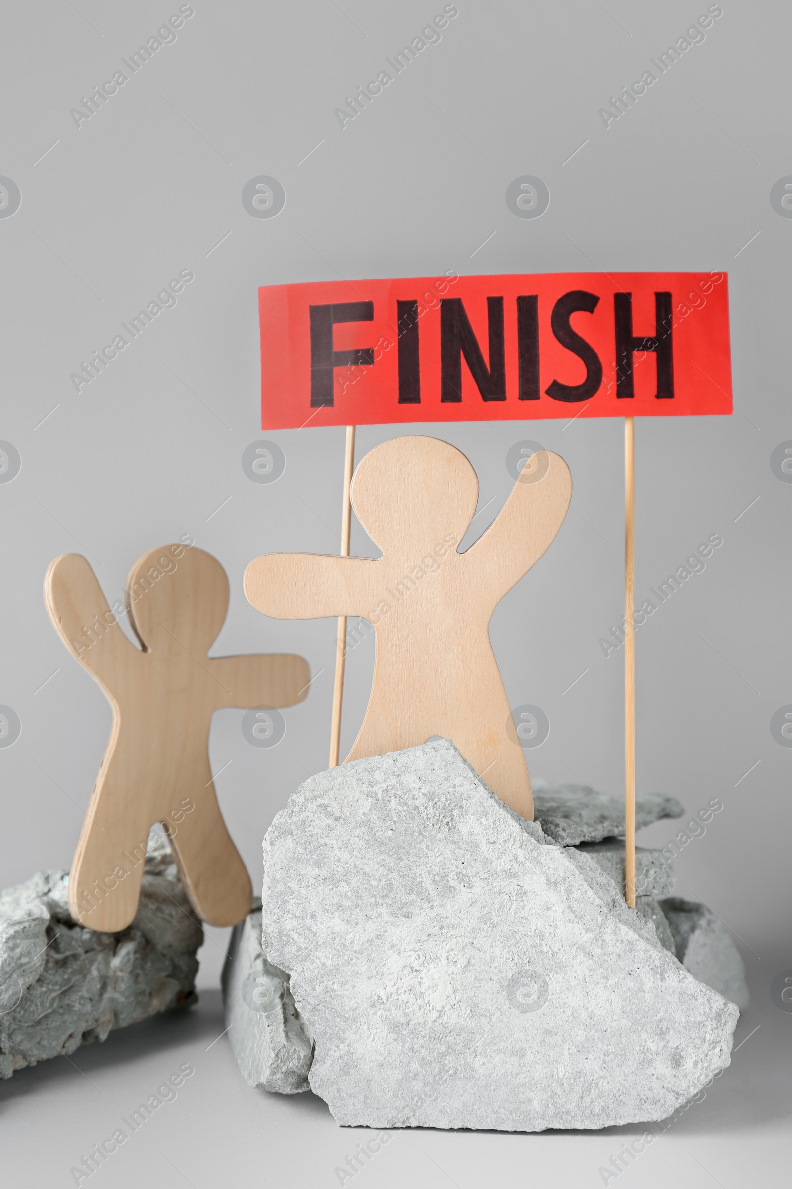 Photo of Competition concept. Wooden human figures on stones and red sign with word Finish against grey background