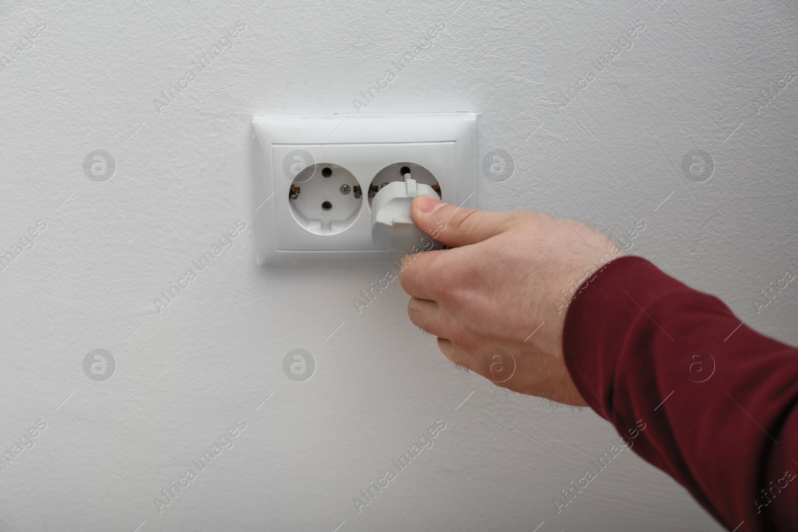 Photo of Electrician inserting plug into power socket on white background, closeup