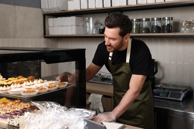 Seller taking tasty tartlet from showcase in bakery shop