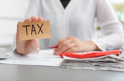 Photo of Woman holding card with word TAX at table
