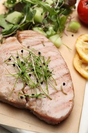 Photo of Delicious tuna steak with microgreens on parchment paper, closeup