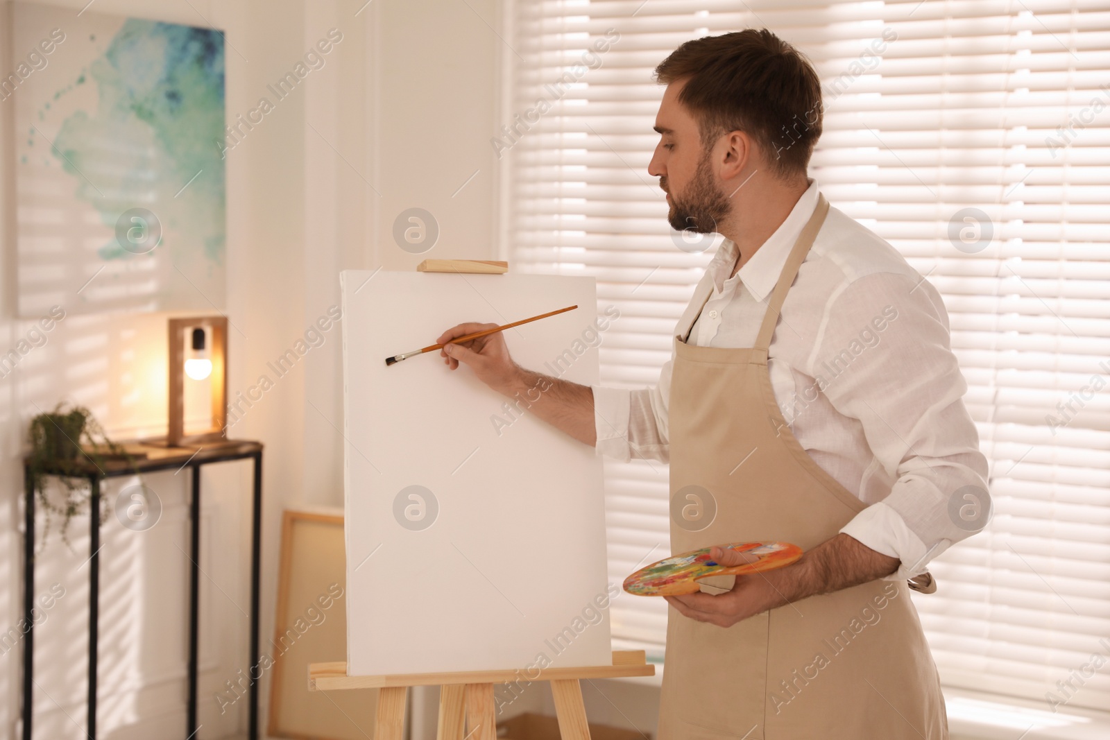 Photo of Young man painting on easel with brush in artist studio