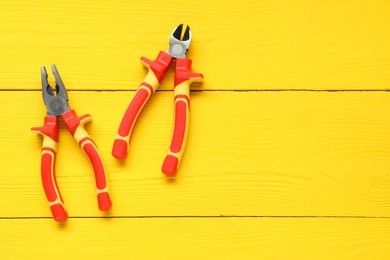 Pliers on yellow wooden table, flat lay. Space for text