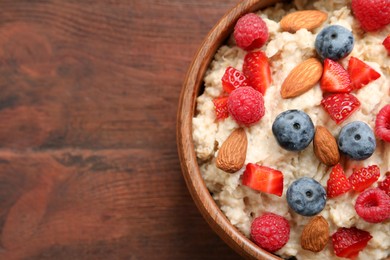 Photo of Tasty oatmeal porridge with berries and almond nuts in bowl on wooden table, top view. Space for text