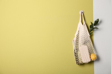 Photo of Conscious consumption. Net bag with eco friendly products hanging on olive wall, space for text