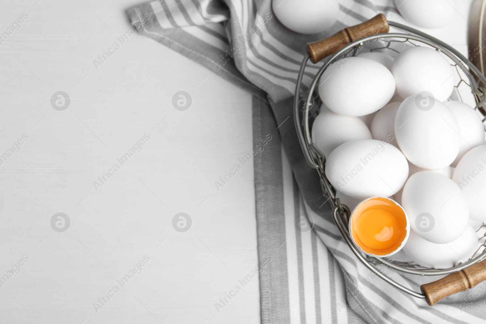 Photo of Many raw chicken eggs in metal basket on white wooden table, flat lay. Space for text