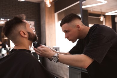 Professional hairdresser working with client in barbershop