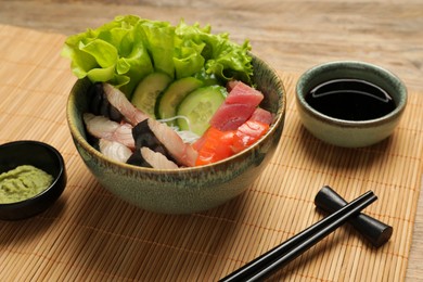 Photo of Delicious mackerel, salmon and tuna served with funchosa, cucumbers, lettuce, wasabi and soy sauce on wooden table, closeup. Tasty sashimi dish