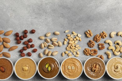 Tasty nut butters in bowls and raw nuts on light grey background, flat lay