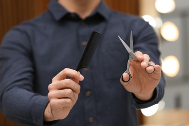 Photo of Hairstylist holding professional scissors and comb in beauty salon, closeup