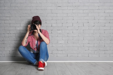 Young female photographer with camera near brick wall