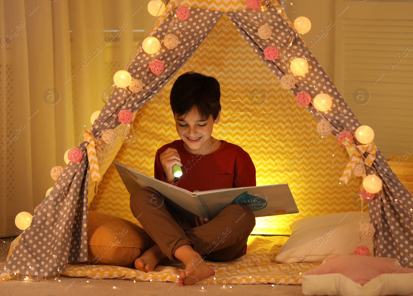 Photo of Boy with flashlight reading book in play tent at home