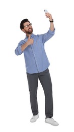 Photo of Smiling man taking selfie with smartphone and showing thumbs up on white background