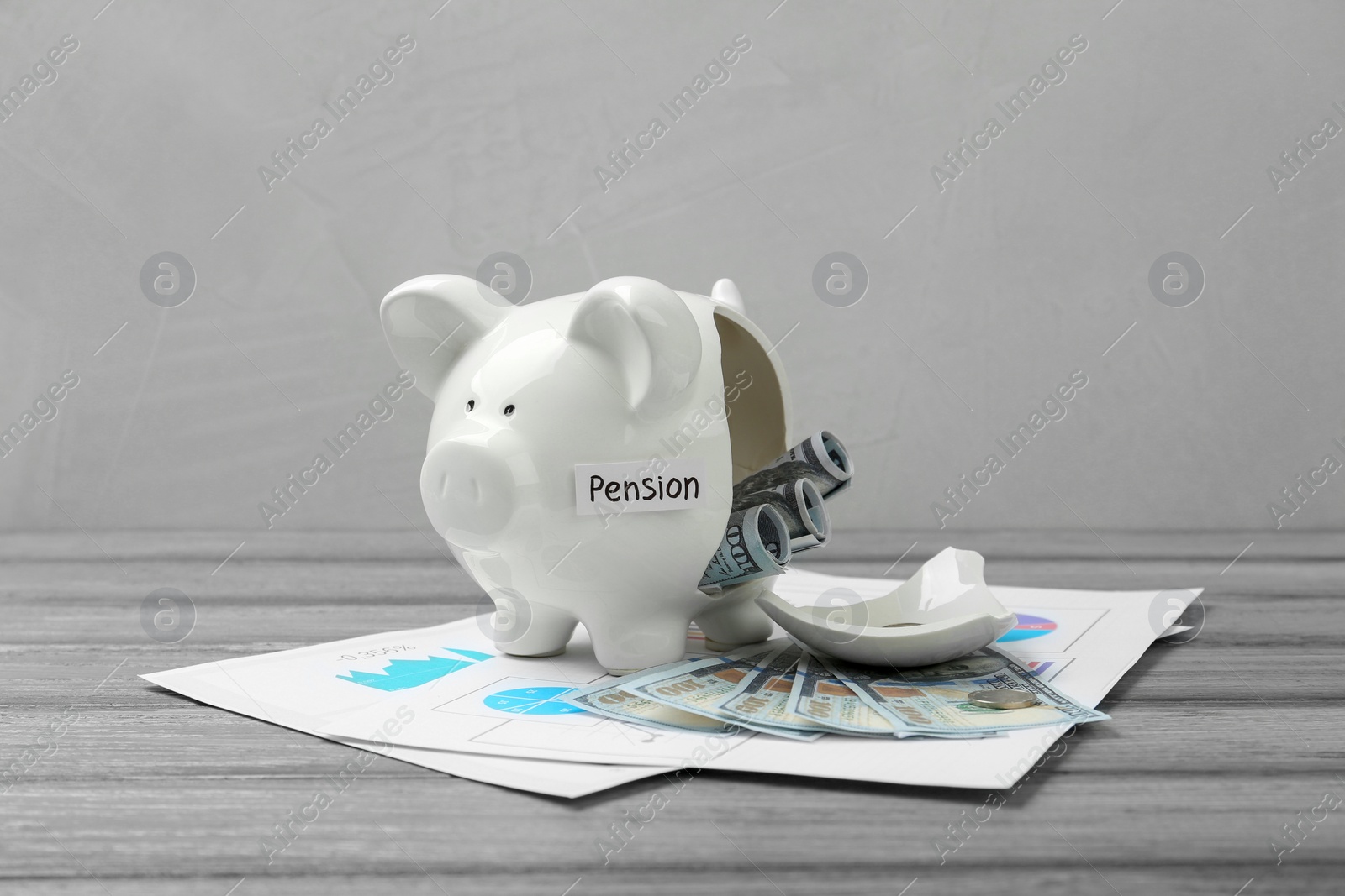 Photo of Broken piggy bank with word Pension, dollar banknotes and diagrams on grey wooden table. Retirement savings