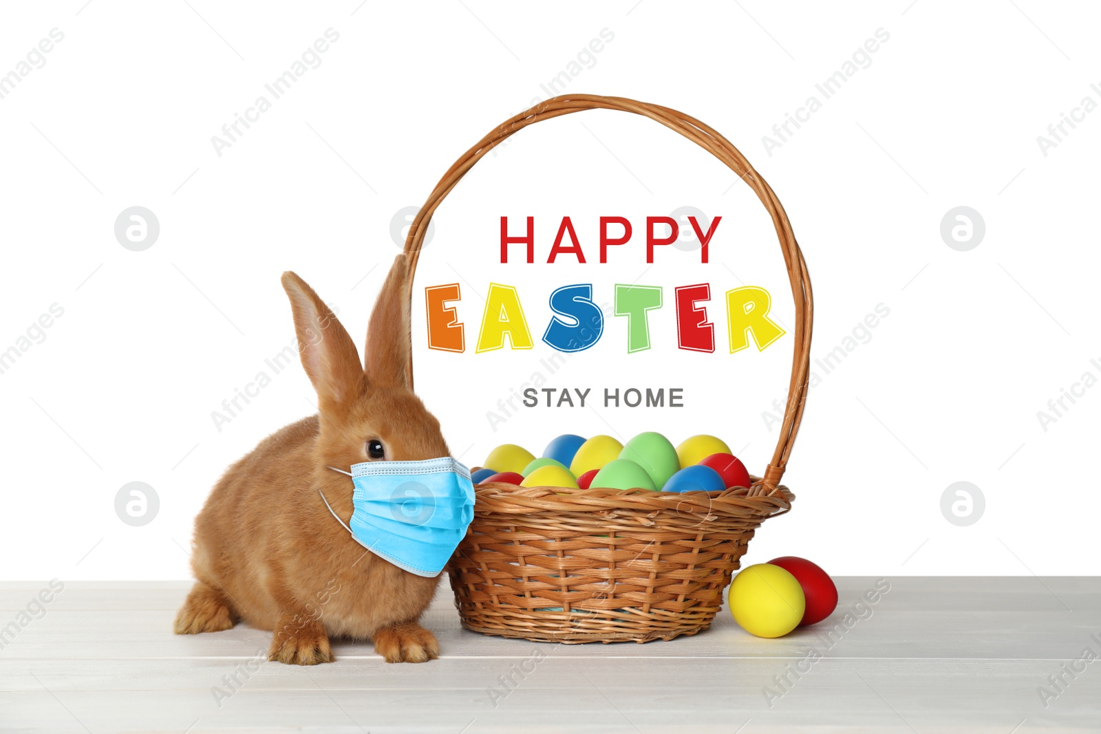 Image of Text Happy Easter Stay Home and cute bunny in protective mask on white table. Holiday during Covid-19 pandemic