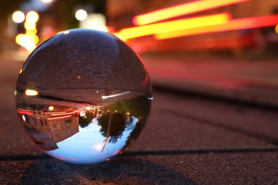 Photo of Beautiful city street, overturned reflection. Crystal ball on asphalt road at night, closeup. Space for text