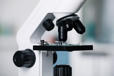 Modern medical microscope with glass slide on blurred background, closeup