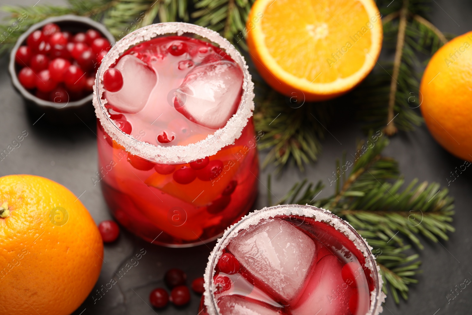 Photo of Tasty cranberry cocktail with ice cubes in glasses on dark gray table, closeup
