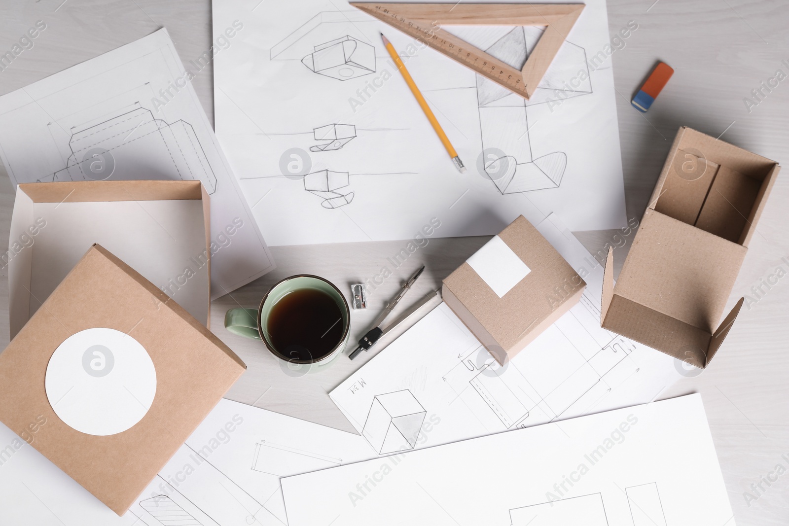 Photo of Creating packaging design. Drawings, boxes, coffee and stationery on light wooden table, flat lay