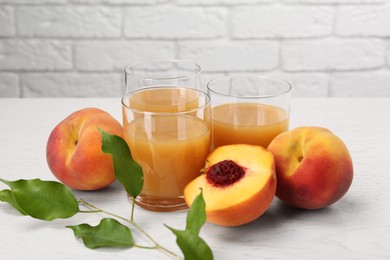 Glasses of delicious peach juice, fresh fruits and leaves on white wooden table