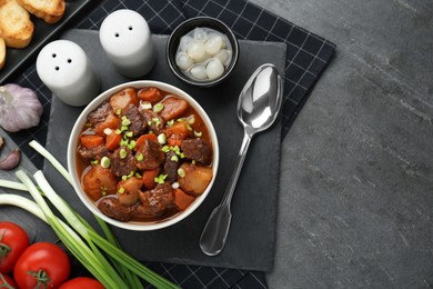Photo of Delicious beef stew with carrots, green onions and ingredients on grey table, flat lay. Space for text