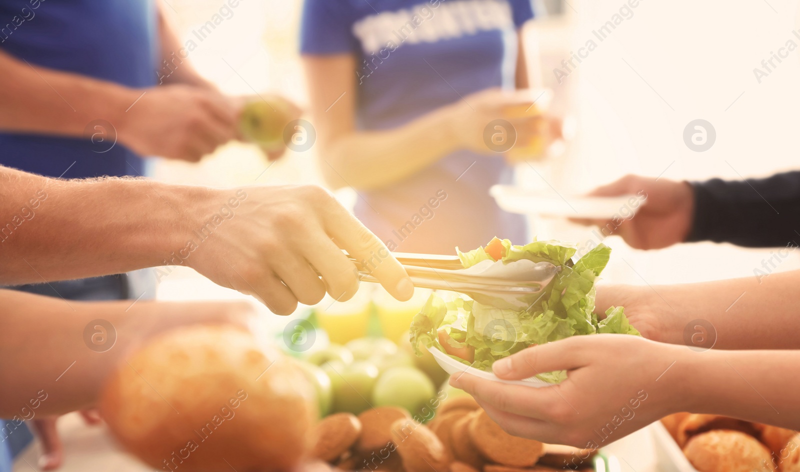 Image of Volunteers serving food to poor people in sunlit room, closeup