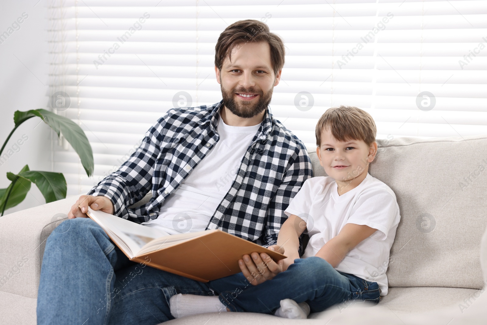 Photo of Family portrait of happy dad and son with book on sofa at home