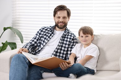Photo of Family portrait of happy dad and son with book on sofa at home
