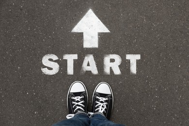 Image of New beginnings. Woman standing near arrow and word Start on asphalt, top view
