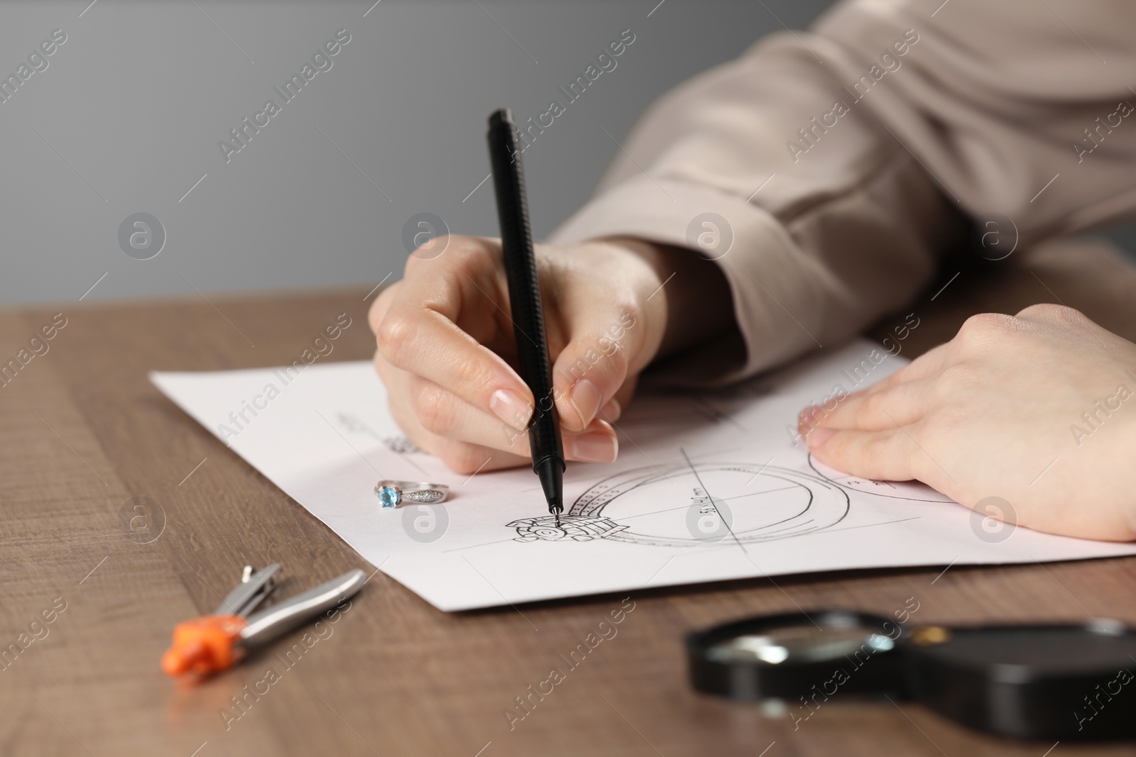 Photo of Jeweler drawing sketch of elegant ring on paper at wooden table, closeup